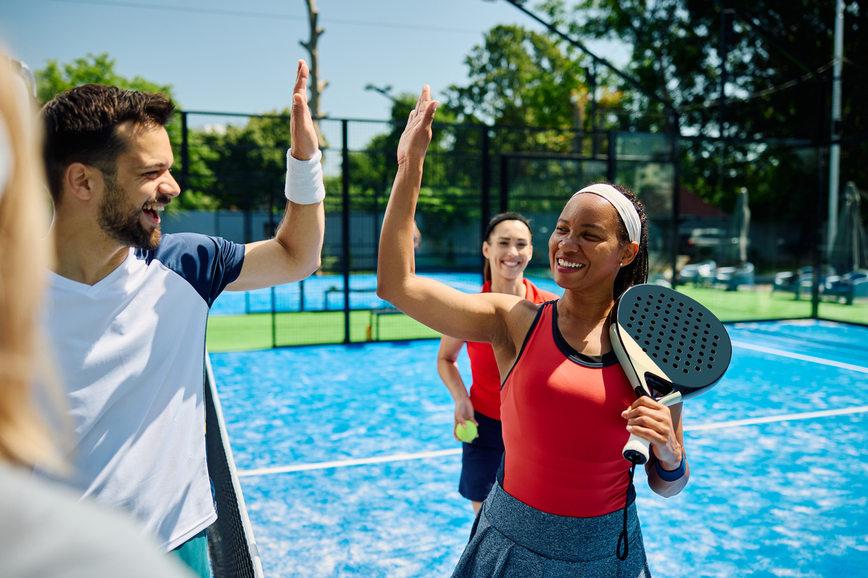 Happy padel players high-fiving on a blue court