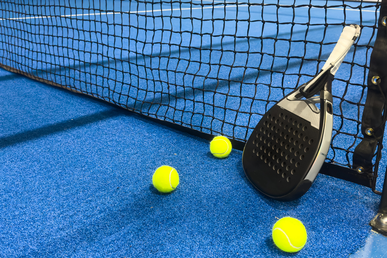 Padel racket and tennis balls on a blue padel court